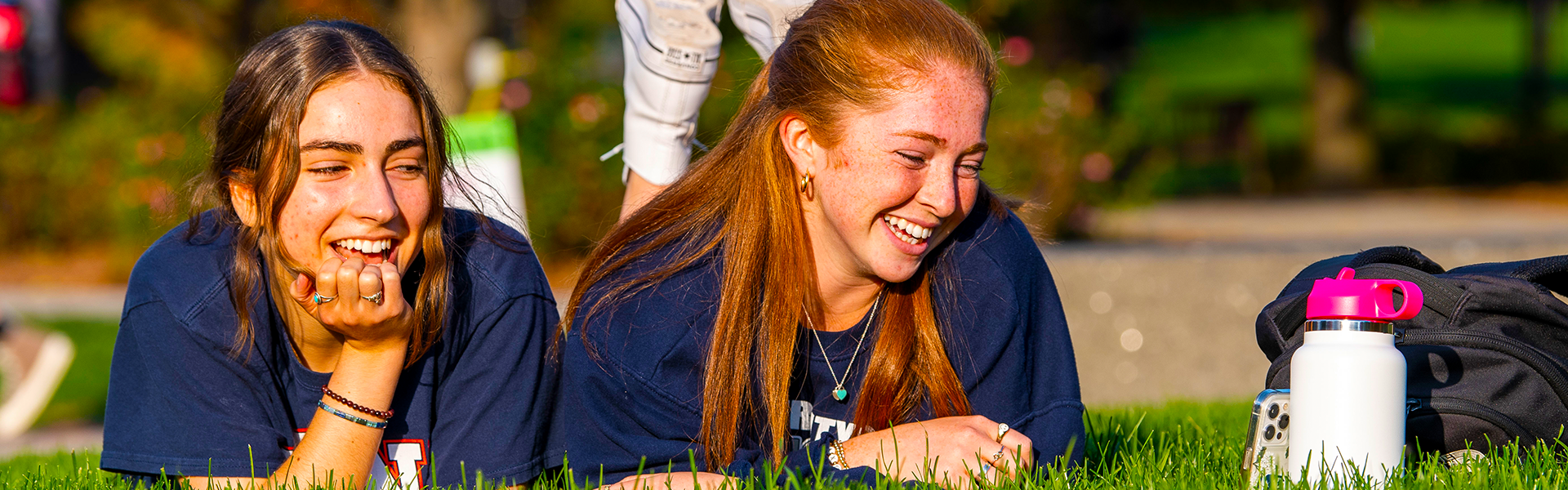 students laying in the grass, laughing at a smartphone screen