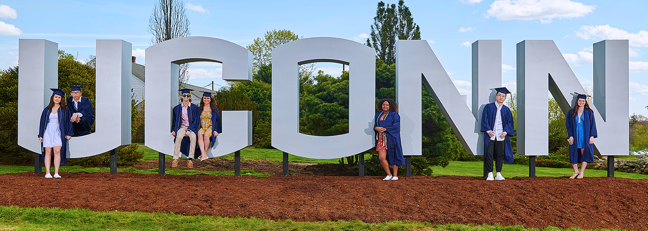 uconn students pose in camp and gown at the uconn sign on route 195